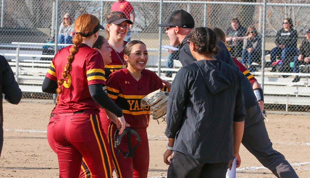 Softball player congratulated by teammates and coach.