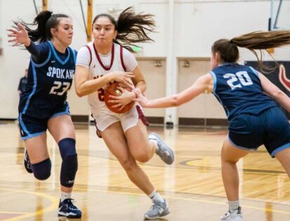 Female basketball player drives between two defenders