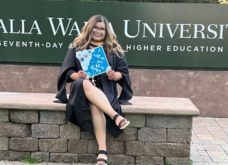 Jasmine Aldaco poses in front of Walla Walla University's sign on her graduation day in 2022