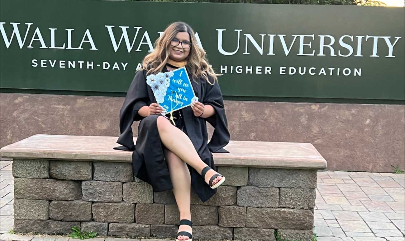 Jasmine Aldaco poses in front of Walla Walla University's sign on her graduation day in 2022