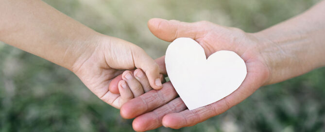 A larger hand holding a heart and a child's hand