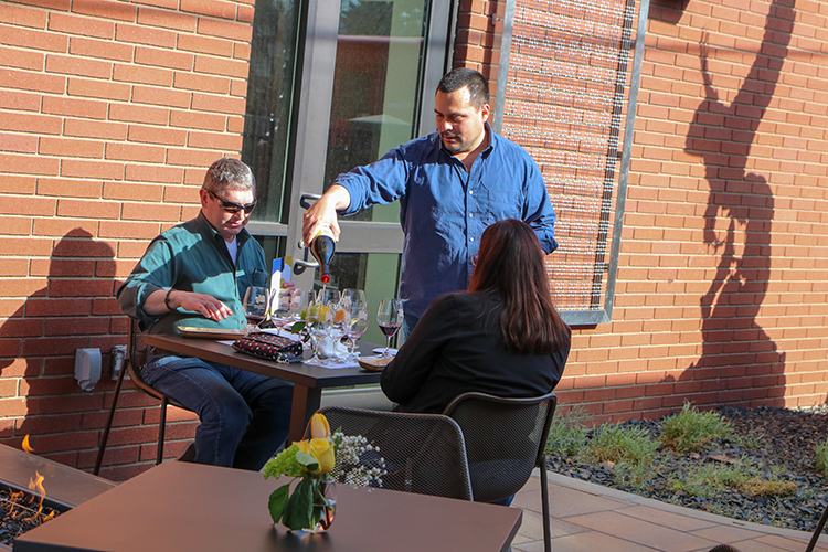Server at YVC Tasting Room pours local wine to patrons in the outdoor seating area.